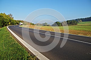 Asphalt road in the countryside, white truck coming around in the distance the bend