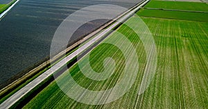 Asphalt road crosses boundless fields with channel in spring