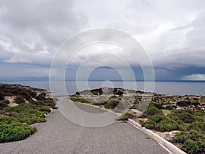 Asphalt road through deserted area leading to stormy sea