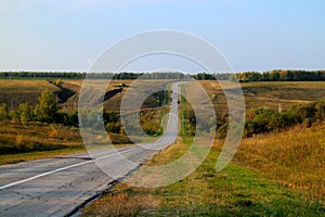 Asphalt road disappearing into horizon on background of meadows forests and blue sky