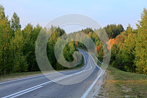 Asphalt road disappearing into horizon on background of meadows forests and blue sky