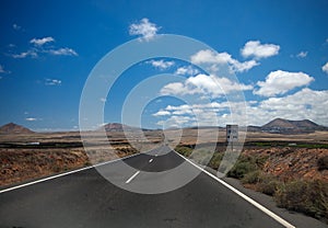 Asphalt road disappearing over the horizon through volcano mountain hillsides. Radar sign. White clouds on a blue sky. Lanzarote