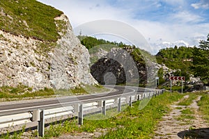 A asphalt road with a dividing strip, an iron security fence and a sign indicating the direction of a sharp turn with red arrows