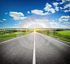 Asphalt road in field under blue sky