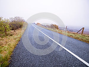 Asphalt road and fields in country side in a fog. Dangerous driving conditions with low visibility and wet road surface. Mist over