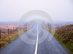 Asphalt road and fields in country side in a fog. Dangerous driving conditions with low visibility and wet road surface. Mist over