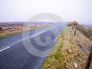 Asphalt road and fields in country side in a fog. Dangerous driving conditions with low visibility and wet road surface. Mist over