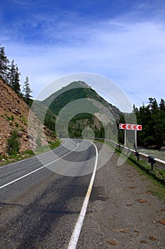 An asphalt road goes around a rocky mountain, fenced by signs and signs