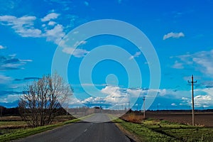 Asphalt road among the green field, blue sky with white clouds. Spring background horizontal photo, travel concept