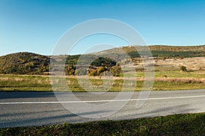 Asphalt road through the green field and clean blue sky in autumn day.