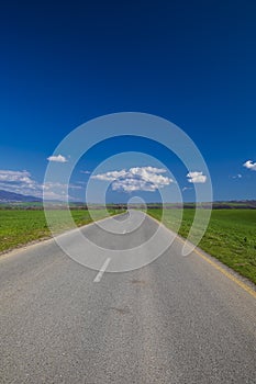 Asphalt road between green fields