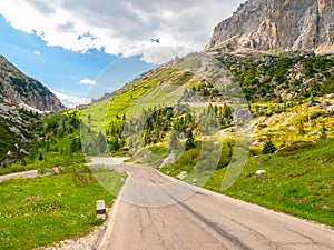 Asphalt road, green meadows and dolomite rocks at Passo Falzarego, Dolomites, Italy