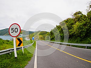 Asphalt road on hill with limit speed sign board sea island at phuket Thailand