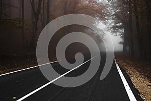 Asphalt road leading to the top of the hill at autumn in dense fog with low visibility.