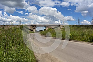 Asphalt road leads to the railway bridge, sky, clouds, grass