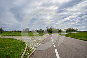 An asphalt road with markings goes away to the horizon. Low section shot, overcast weather, and low clouds in the background.