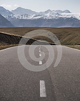 Asphalt road with markings in the mountains against the background of a valley and a mountain range with snow cover and glaciers