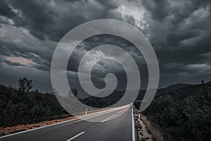 Asphalt road panorama in countryside on cloudy day. Road in forest under dramatic cloudy sky.