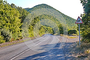 Asphalt road resting on a mountain with a sign showing the turn with green trees on the roadside