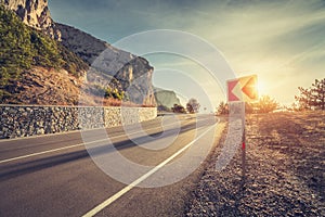 Asphalt road and road sign in mountains at sunrise