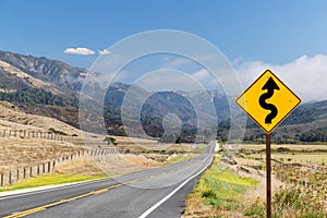 Asphalt road, sign and country landscape with sunny sky