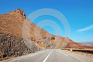 Asphalt road , small Atlas mountains and rock hills both sides, clear sky above - typical landscape in Southern Morocco