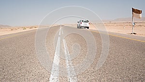 Asphalt road straight in the desert in the south of Oman with a parked 4x4 vehicle