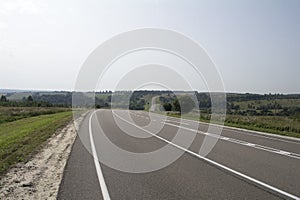 Asphalt road with white markings going through hilly countryside.