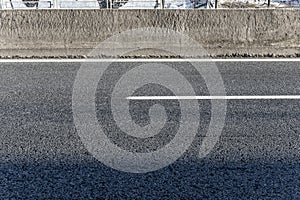 Asphalt of a road with white paint separating the lanes and a concrete wall separating the carriageways