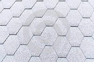 Asphalt roofing shingles texture covered with light snow. House roof shingles covered with frost. Snow covered roof of the house.