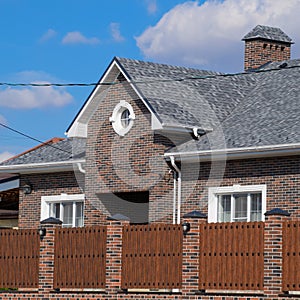 Asphalt shingle. Decorative bitumen shingles on the roof of a brick house. Fence made of corrugated