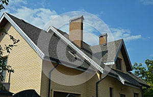 An asphalt shingled roof with skylights, attic windows, chimneys, fascias, and a roof gutter. A close-up of a gray double-pitched