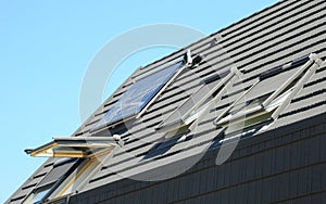 Asphalt shingles house roof top with attic skylights, open windows, dormer, solar water heater and solar panels photo