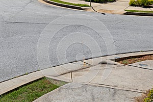 Asphalt street bordered by formed curbs, sidewalks, and grass, handicap ramp access