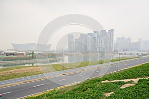 Asphalted road and sideway along river with city buildings in light winter mist