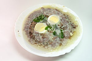 Aspic jelly with meat, eggs and fresh parsley, made with thick and rich bone broth, frozen in elegant white dinner plate.