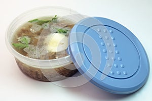 Aspic with meat, eggs and fresh parsley, made with thick and rich stock, in round plastic food container with a blue lid