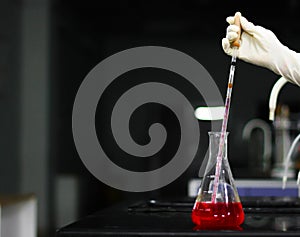 Aspirating a red chemical on a glass conical flask with a pipette in a chemistry lab photo