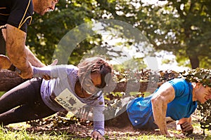 Assault course competitor helping others crawl under nets