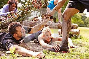 Assault course competitor helping others crawl under nets