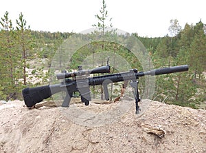 Assault rifle on the background of pine forests and sand