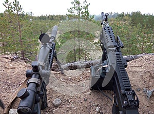 Assault rifle and machine gun on the background of pine forests and sand