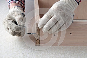 Assembling  furniture box, gloved hands tighten  screw with  key