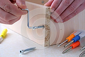 Assembling furniture box, mens hands tighten  screw with  key, close-up