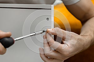 Assembling furniture at home. Tightening the bolt with a screwdriver. Cabinet installation. A man in a white T-shirt is assembling