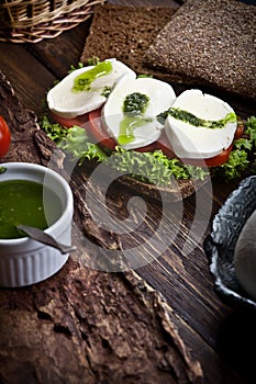 Assembling sandwich with mozzarella, tomatoes, pesto and green salad, on rustic wooden table