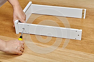 The assembly worker tightens into a wooden drawer made of particle board with a screwdriver, ready-to-assemble furniture