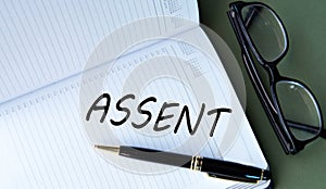 ASSENT - word in notebook on green background with glasses and pen photo