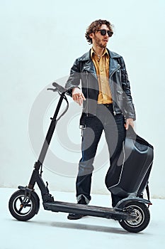 Assertive and rich young man posing on a scooter in a bright studio, looking cool