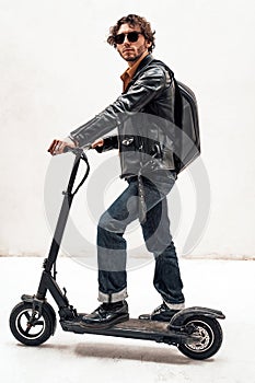 Assertive and rich young man posing on a scooter in a bright studio, looking cool